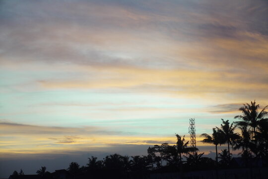Pastel sunset sky over tropical tree silhouettes and telecommunication tower