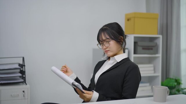 Young professional woman reviewing document with pen in modern office environment wearing glasses and formal attire