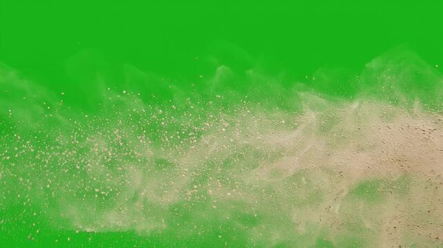 Brown sand particles exploding horizontally across a bright green screen background for visual effects