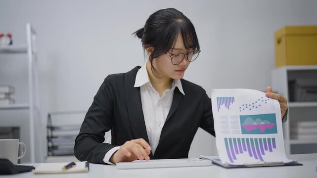 Young professional woman sitting at desk in modern office working focused on computer keyboard with glasses and formal attire