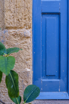 Vibrant Royal Blue Painted Wooden Door Beside Textured Limestone Wall with Green Plant Leaves