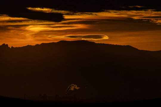 Industrial smoke rising under dramatic sunset mountains
