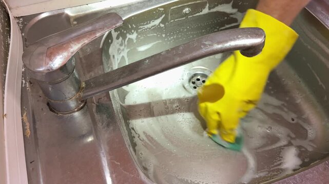 Top View of Hand in Yellow Glove Scrubbing Kitchen Sink