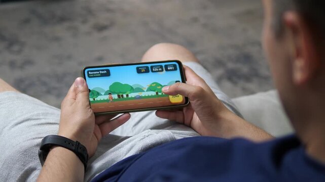 Young man plays a colorful endless runner on a smartphone, capturing casual mobile gaming, digital entertainment and the growing popularity of quick play experiences.