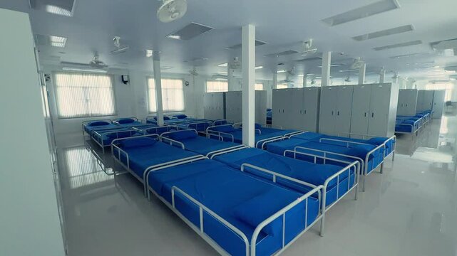 Interior shot of a clean and organized military barracks room with rows of blue beds and white lockers.