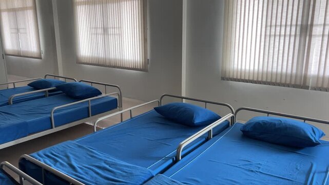 Interior shot of a clean and organized military barracks room with rows of blue beds and white lockers.
