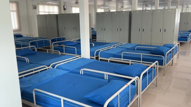 Interior shot of a clean and organized military barracks room with rows of blue beds and white lockers.