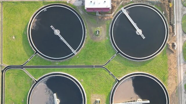 Aerial view of water treatment facility showcasing circular tanks and machinery. Sewerage system surrounded by greenery. Modern industrial plant of big city. Ecology friendly factory