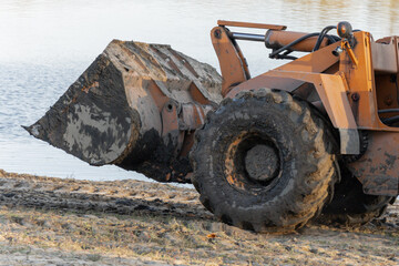Orange wheel loader bucket working near water at industrial construction site copy space © Sveta