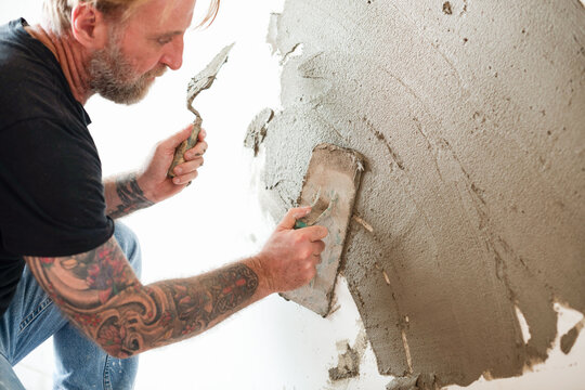 Caucasian man plastering wall with a trowel during home renovation
