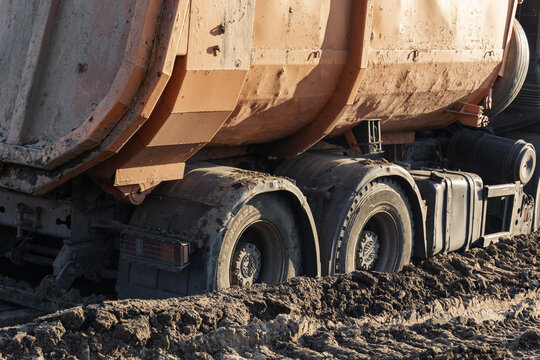 Orange dumper truck wheels stuck in deep mud at industrial construction site copy space