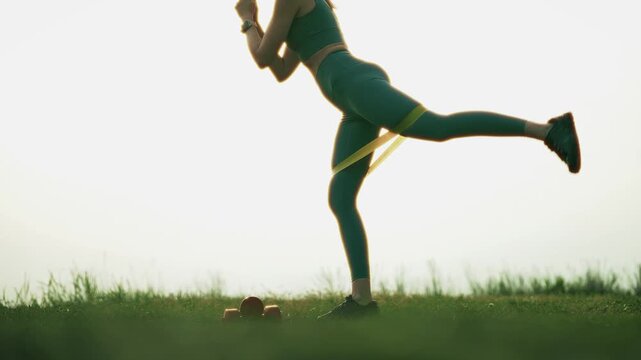 Athlete Performing Leg Exercises With Resistance Band In Grass Field. Outdoor Training