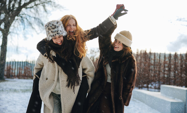 Friends watch women enjoy a piggyback ride in snow