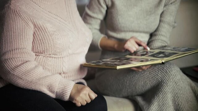 Mother And Daughter Looking Through Old Photo Album While Sitting Together 