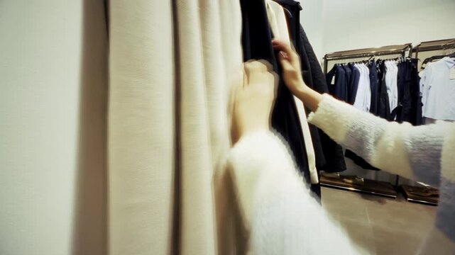 Shopper Choosing Coat From Hanger While Browsing Collection In Store