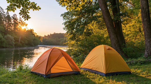 Orange and yellow camping tents beside a forest river in a peaceful sunset setting