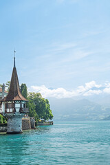 Historic turret tower on the shore of Lake Thun in Switzerland featuring traditional timber architecture against a backdrop of scenic Alpine mountains © Ilja