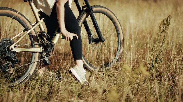 Cyclist Applying Tick Repellent Spray On Leg While Standing Next To Bicycle In Grass Field