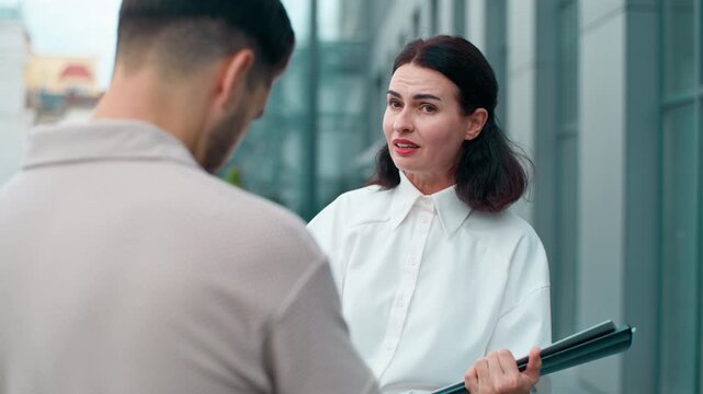 Back view sad man businessman listening Caucasian businesswoman irritated annoyed with business documents talking blaming intern talk aggressive in city. Two workers problem communication in downtown
