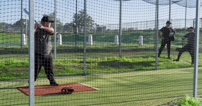 Diverse males capped practicing in park batting cage, batter on orange mat holding bat, copy space