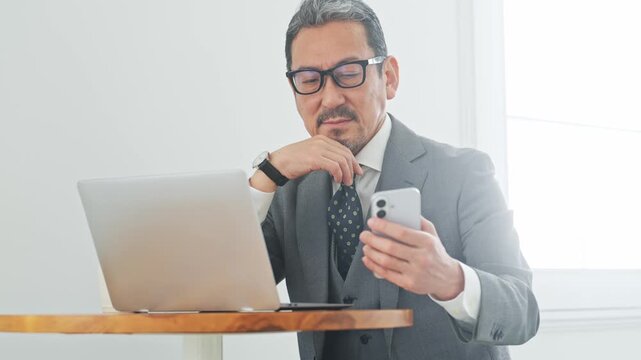 A middle-aged male business professional struggling with issues while using his smartphone and laptop. Dissatisfaction, questions, apps, failures, disappointments, social media.