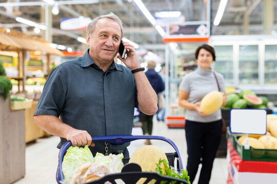 Mature man talking on phone in grocery store with groceries in cart