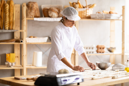 Elderly woman baker rolls out dough