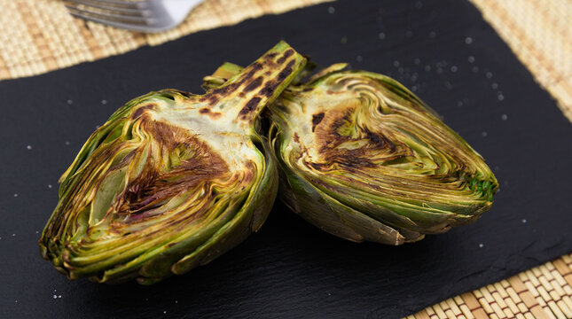 cooked fried halves artichokes on black stone board