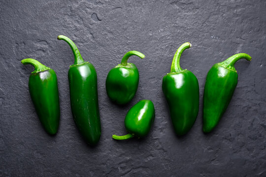 Group of jalapeno peppers arranged on dark stone surface minimal style. Fresh green chili lineup natural background