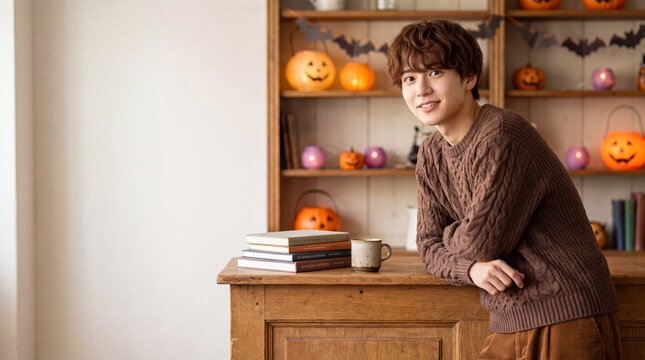 ハロウィン飾りの棚の前で微笑むブラウンニットの男性 | 温もり