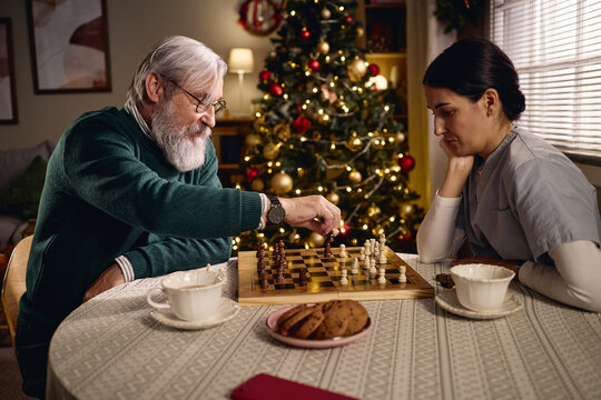 Senior Caucasian man playing chess with female caregiver during Christmas holidays, representing eldercare companionship. Useful for assisted living and nursing home marketing
