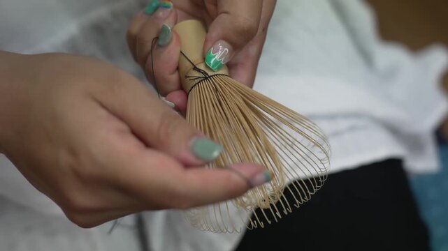 Close up of hands tying thread around the bamboo tines of a handmade matcha whisk