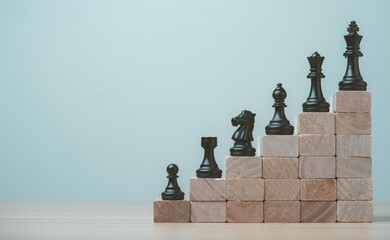 Black chess pieces rising on wooden block steps toward the king, symbolizing business strategy, leadership career growth, strategic planning to achievement and success concept. © Dilok