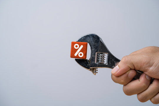 Interest rate adjustment concept with hand holding adjustable wrench gripping a wooden percentage symbol representing financial control of banking policy and borrowing costs regulation.