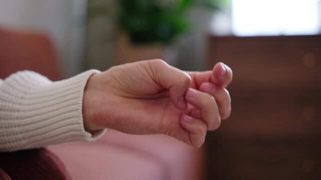 Close-up of a nervous woman fidgeting with her fingers, picking at nails and hangnails while experiencing anxiety and stress at home.