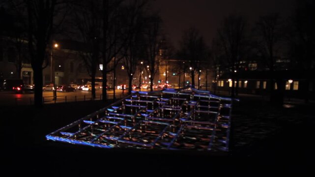 Colorful illuminated structure in a park beside a road at night