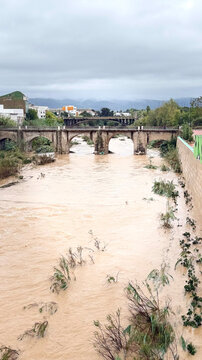 Floodwater surging beneath a stone bridge as a swollen river inundates the urban riverbank after recent heavy rainfall