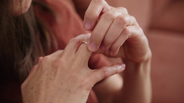 Close-up of a woman nervously twisting and fidgeting with her gold wedding ring, expressing anxiety, relationship doubts, or emotional stress.