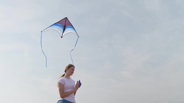 Smiling girl flying a kite with long ribbon tails against a cloudy sky view from below