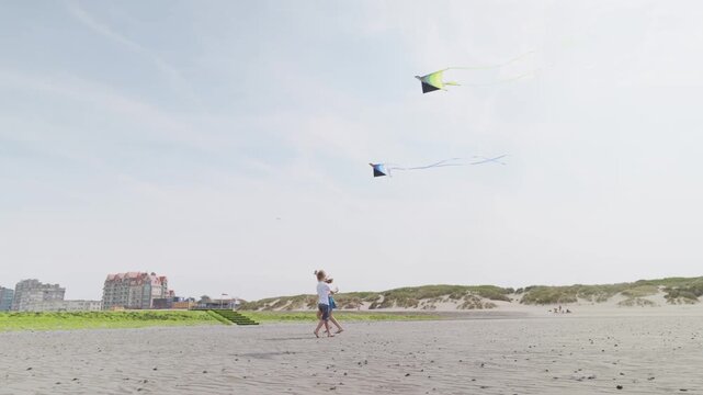 Boy and girl flying kites above a sandy beach with coastal dunes slow motion children on vacation
