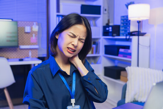 Young Asian businesswoman suffering from neck pain while working on laptop in office.