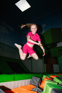 Dynamic action photo of a red-haired girl jumping high in the air above a foam pit in an indoor playground.