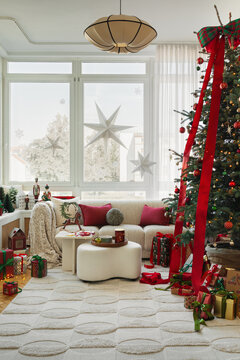 Bright modern living room interior styled for winter holiday with decorated Christmas tree, presents, comfortable sofa, and festive decor elements