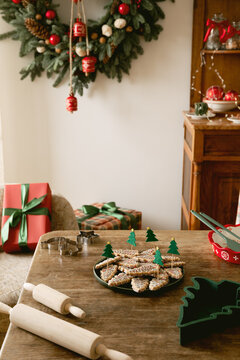 Cozy Christmas table set with homemade tree cookies, wooden rolling pins, gift boxes, and festive wreath decor in a warm rustic winter holiday room