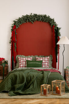 Cozy festive bedroom interior with red wall, green bedding, pine garland, and glowing candles in lanterns, perfect for winter holiday greeting cards and dec