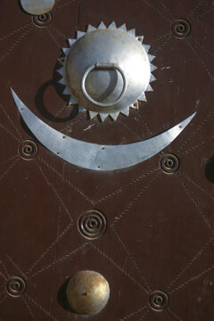 Metal crescent and sunburst door knocker on a brown wooden door with spiral studs, Mopti Region, Djenne, Mali