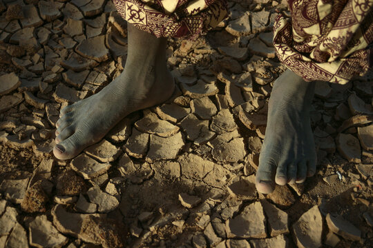 Close up of bare feet standing on cracked dry mud, Mopti Region, Djenne, Mali
