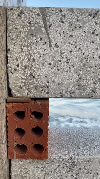 Vertical geometric shot of red brick and terrazzo concrete block wall against a blurry sea with waves in Nha Trang, Vietnam