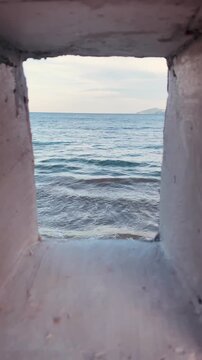 Vertical framed shot of blue sea waves and horizon looking through a concrete wall window in Nha Trang, Vietnam
