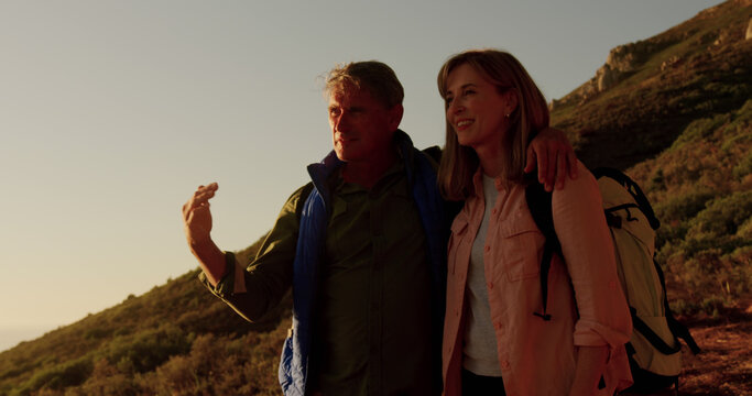 Happy senior caucasian couple hiking in nature embracing and enjoying view at sundown